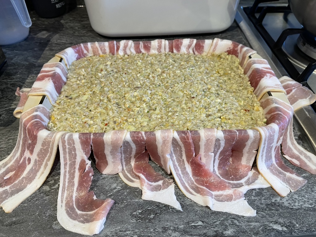 Stuffing mixture in oven dish with bacon draped over the sides